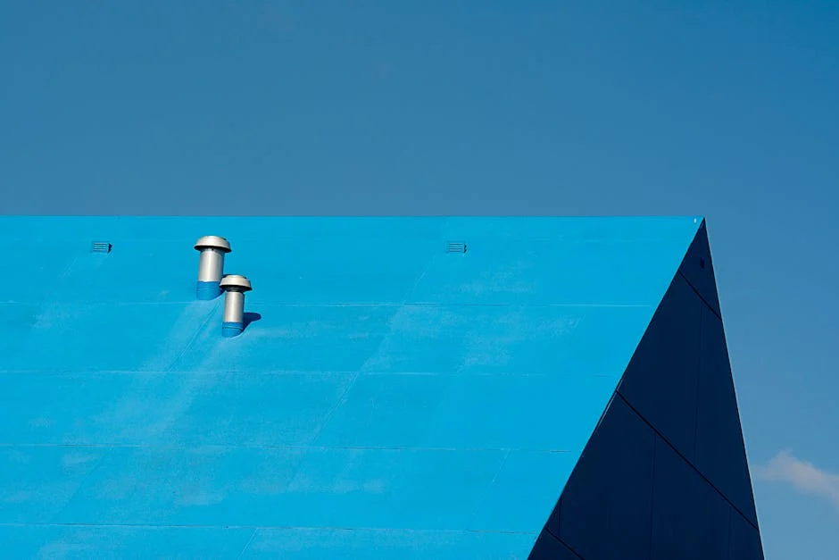 A minimalist photo of a bright blue metal roof with ventilation pipes against a clear sky.