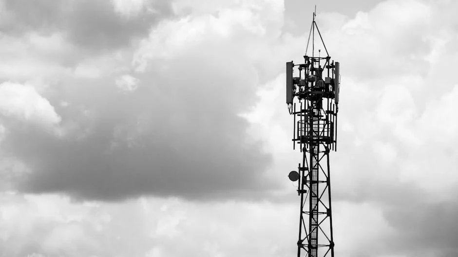 A black-and-white image of a cell tower with clouds in the background.